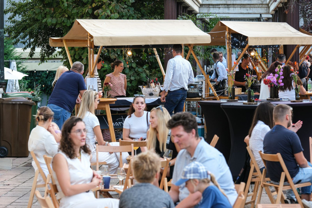 Obiskovalci sedijo in družijo ob kulinaričnih stojnicah na Uličnem festivalu Okusi Posavja v Krškem.