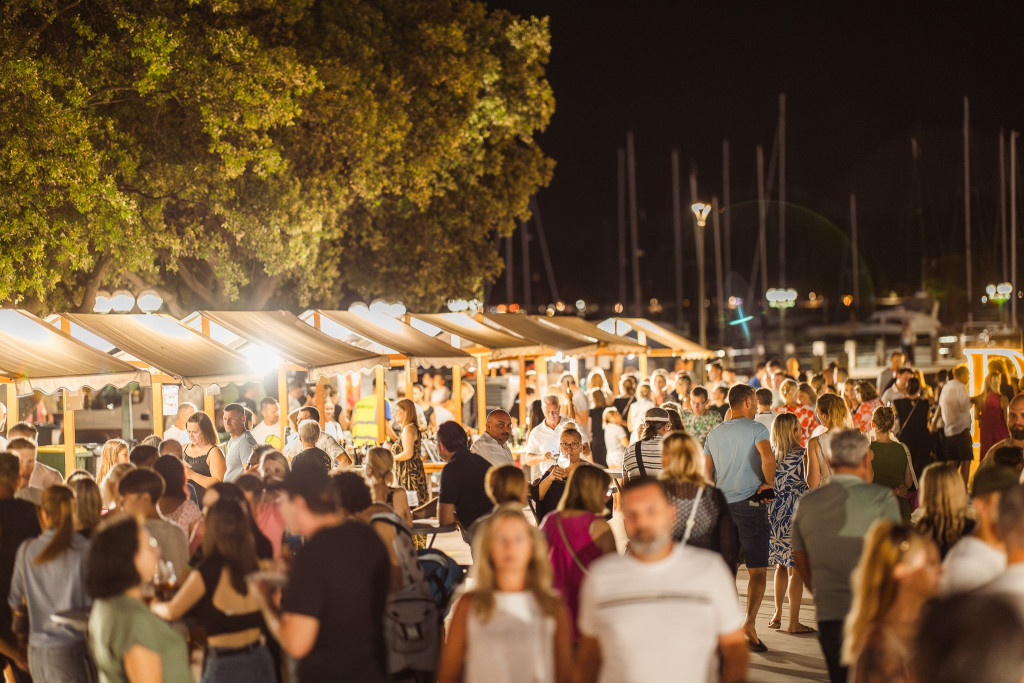 Obiskovalci raziskujejo kulinarične stojnice na dogodku Portoroške noči ob obali.