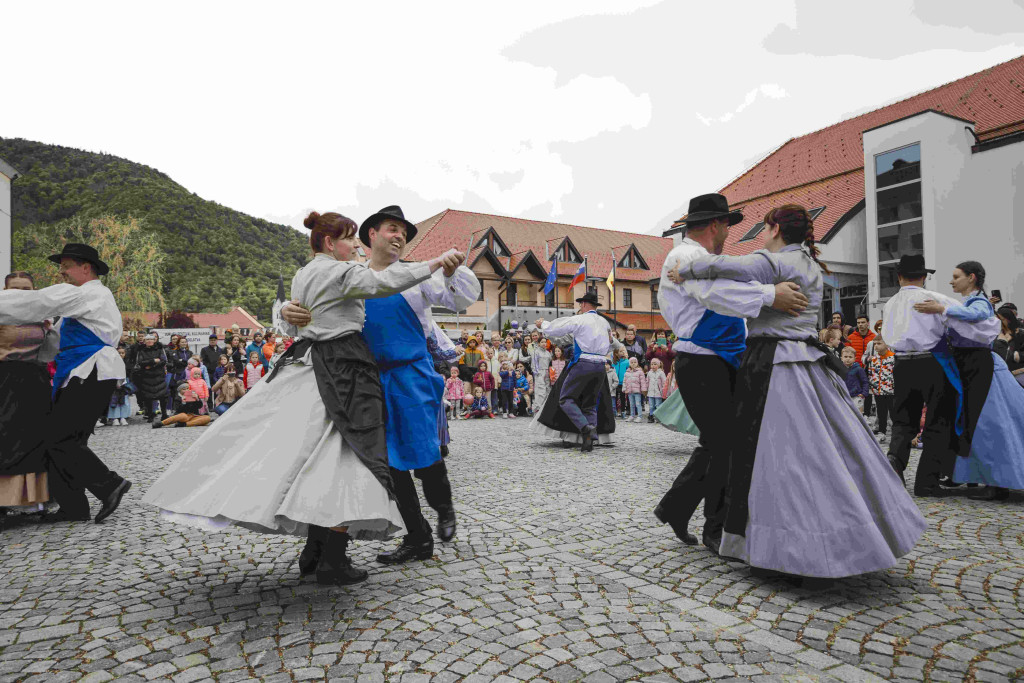 Folklorni plesalci v tradicionalnih oblačilih nastopajo na mestnem trgu pred občinstvom.