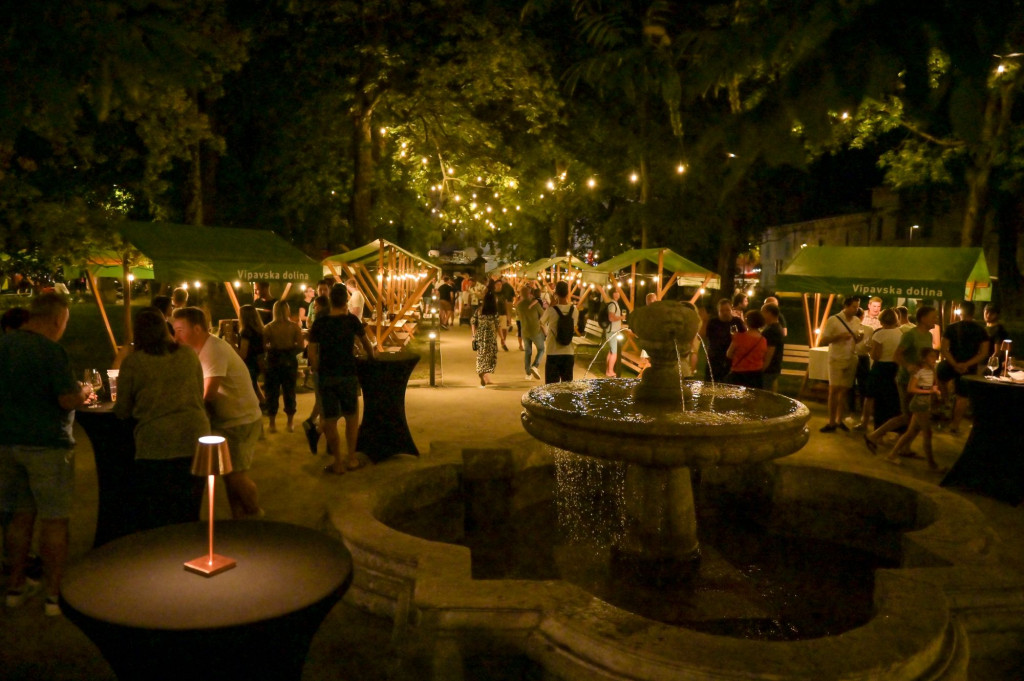 Evening festival scene with illuminated stalls and a fountain in Vipava