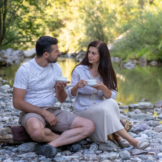 A couple sitting in front of the Idrijca river and drinking welcome drink