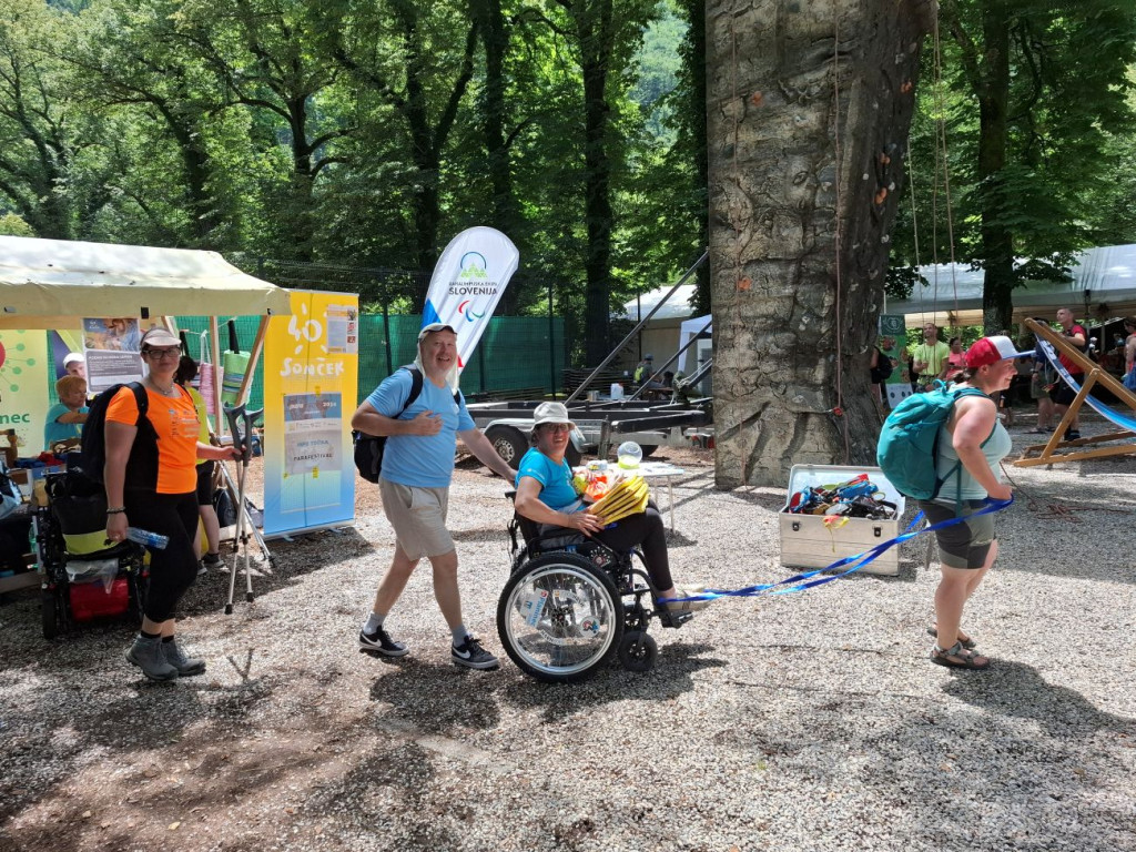 Participants of the Parafestival at the Soča Outdoor Festival, with companions assisting a person in a wheelchair as they move around the festival venue.