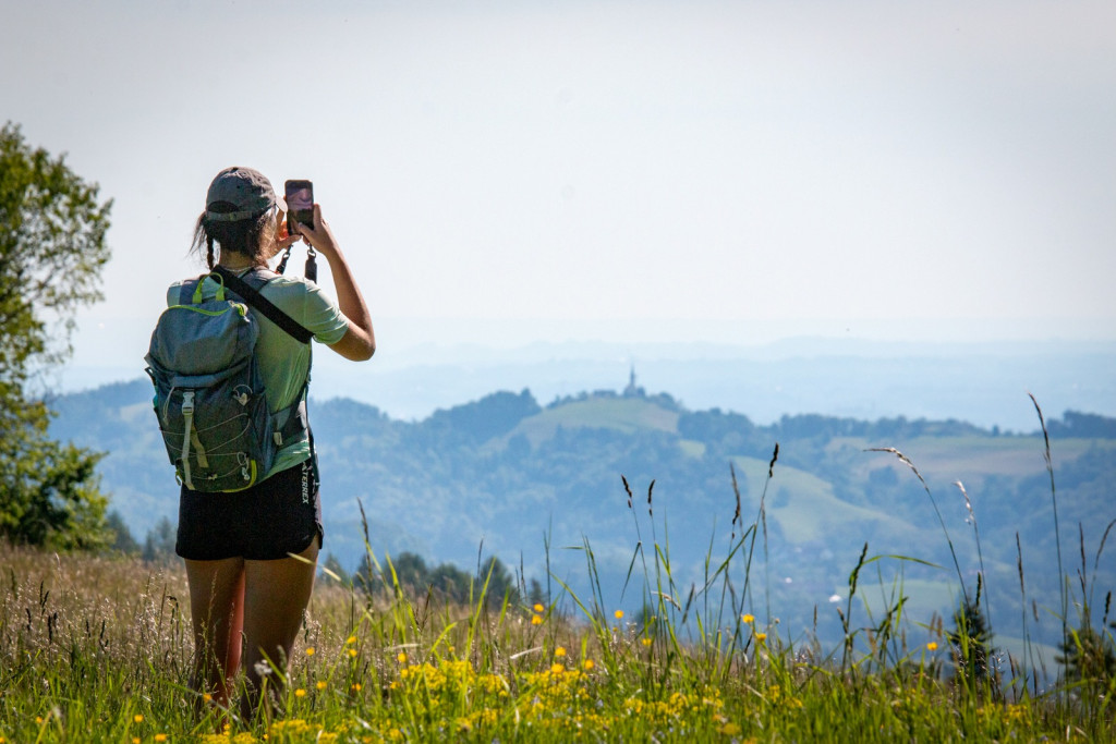 Pohodnica z nahrbtnikom fotografira razgled na gozdnate hribe in dolino.