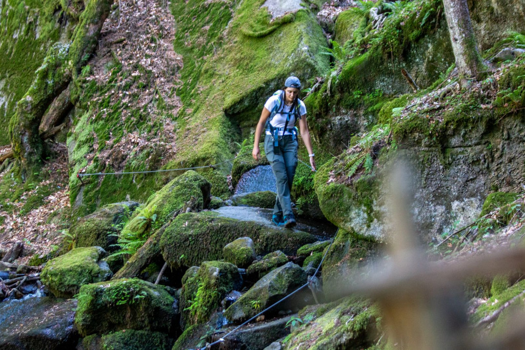 Hiker descending a narrow secured trail between moss-covered rocks.